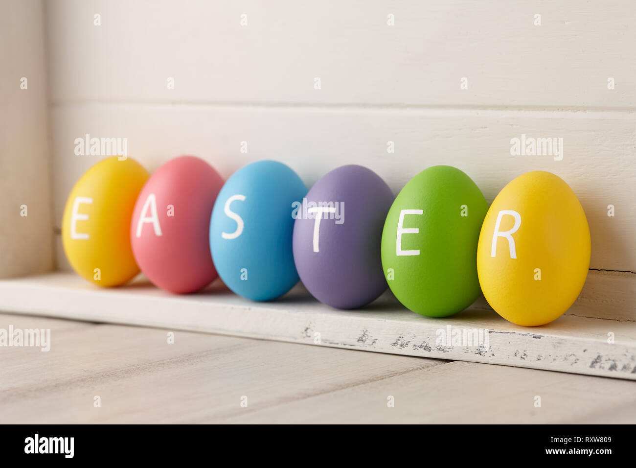 Verniciato colorato uova con lettere disposte in una parola la Pasqua su bianco tavole di legno dello sfondo. Concetto di vacanza. Foto Stock