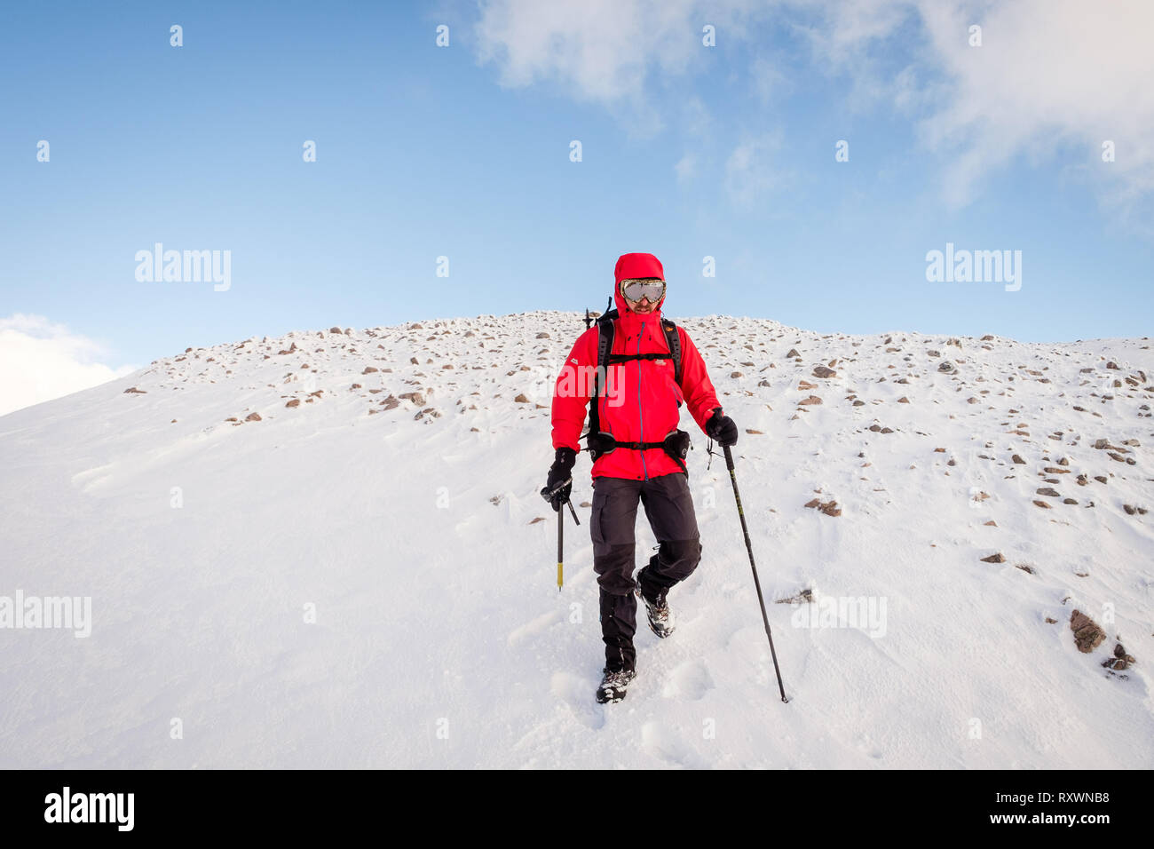 Uomo in camicia rossa, con ghiaccio ax camminando / Alpinismo invernale sulla neve montagna rivestita in Scozia. Modello di rilascio - Garbh Bheinn, Loch Leven Highlands Foto Stock