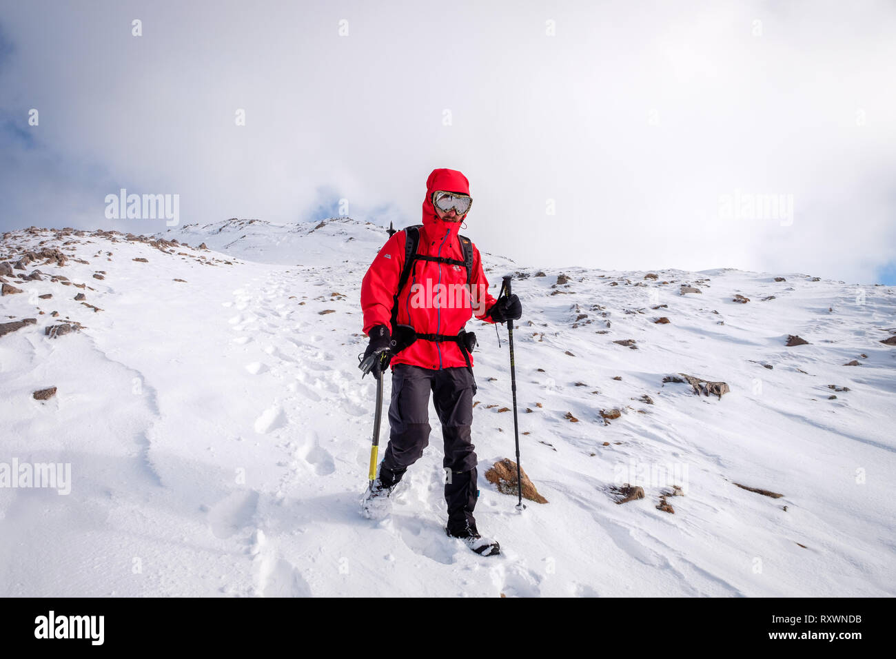 Uomo in camicia rossa, con ghiaccio ax camminando / Alpinismo invernale sulla neve montagna rivestita in Scozia. Modello di rilascio - Garbh Bheinn, Loch Leven Highlands Foto Stock