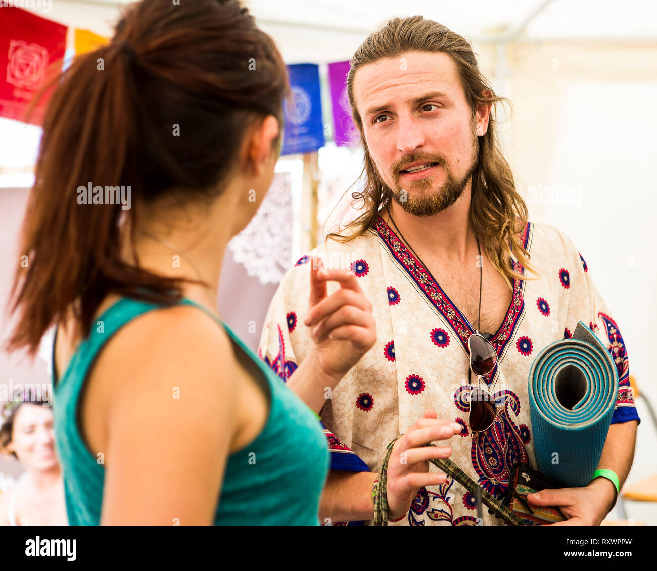 Ragazzo con i capelli lunghi e la barba con un materassino yoga tenuto da una ragazza a nel selvaggio festival, Kent, Regno Unito Foto Stock