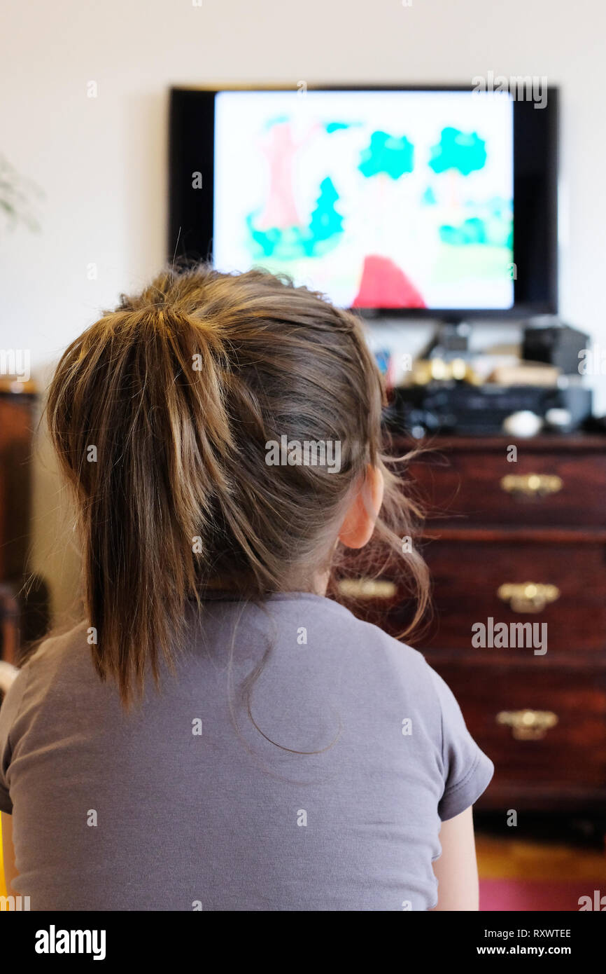 Piccola ragazza sta guardando un fumetto sul TV Foto Stock