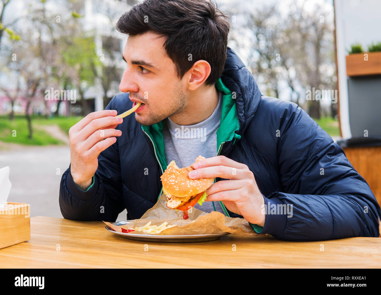 L'uomo mangiare patate fritte con un hamburger in street food cafe Foto Stock