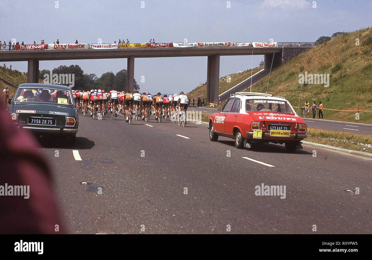 1974 Tour de France, tappa britannica, ciclisti risalendo il Plymouth by-pass, seguita dalla pressa e supporto di vetture Peugeot e guardati da spettatori su un ponte. Foto Stock