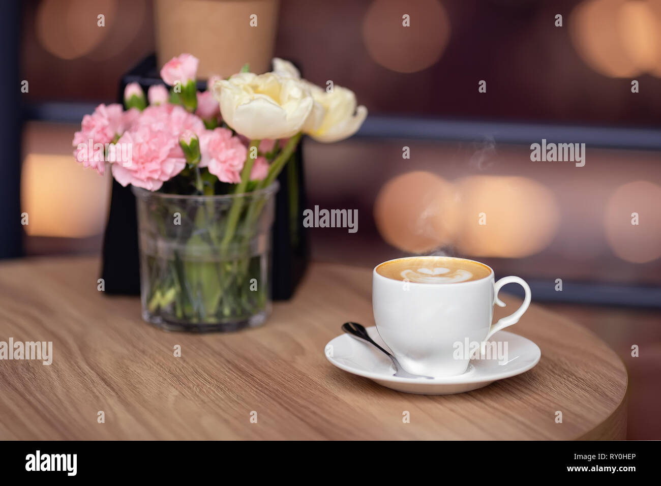White tazza di cappuccino con arte e fiori freschi sul tavolo in cafe Foto Stock