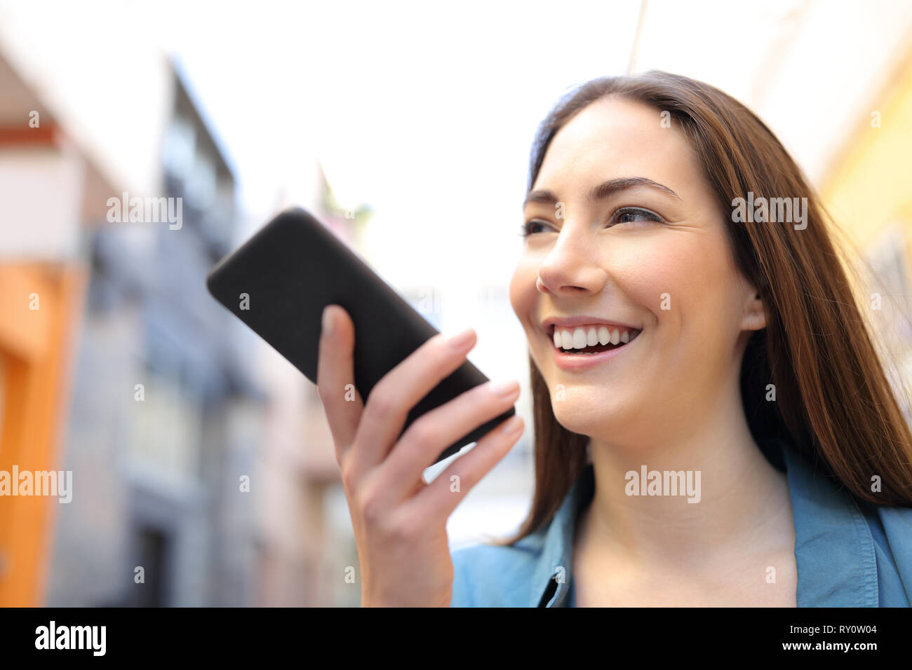 Felice ragazza utilizzando il riconoscimento vocale app su smart phone a piedi in strada Foto Stock