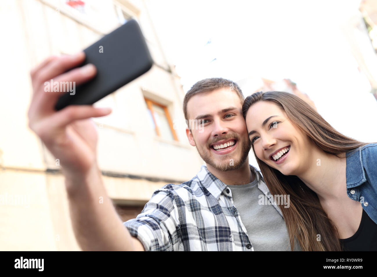 Coppia felice tenendo selfies con smart phone in piedi in strada Foto Stock