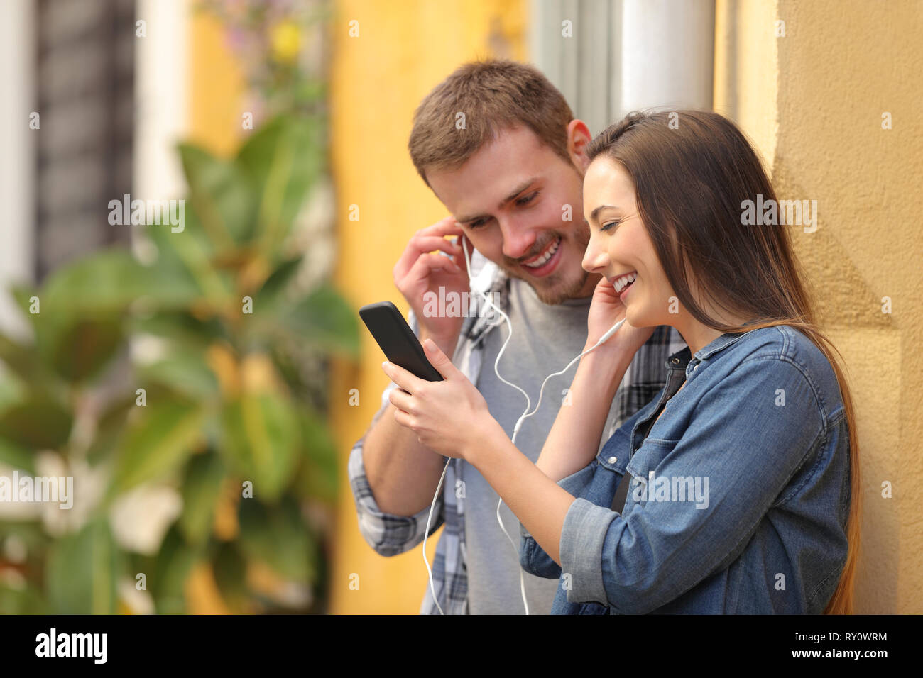 Coppia felice condivisione di auricolari per guardare la media su smart phone in un colorato street Foto Stock