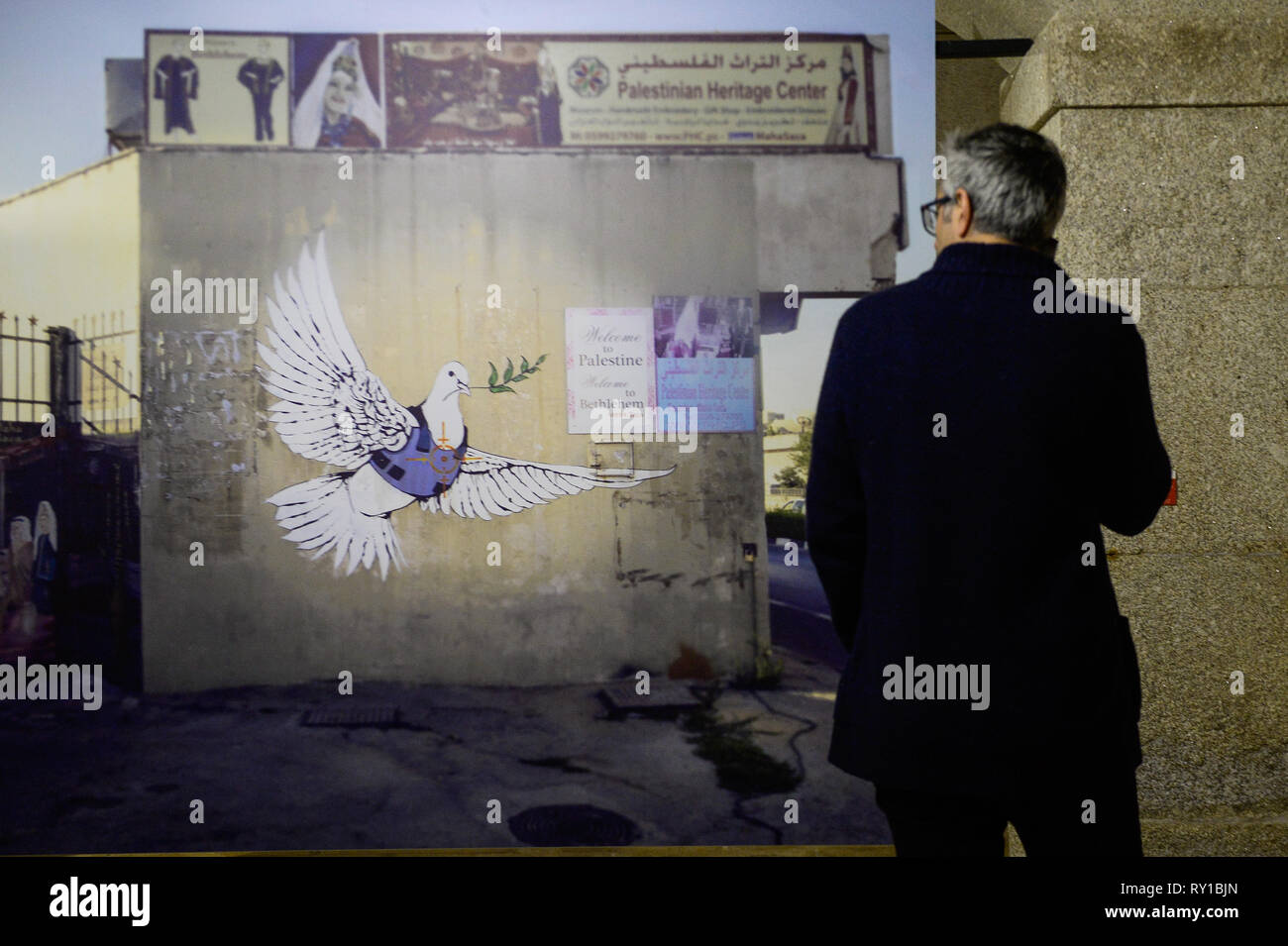 Un visitatore è vedere a piedi da "colomba e Flak Jacket' immagine durante Banksy's Dismaland e altri mostra di Alfandega centro congressi. La mostra include le immagini prese da Barry Cawston dal progetto Dismaland (2015), il ben noto parco a tema creato da Banksy, integrare altre opere che identifica l'artista come "Walled Off Hotel' (2017) o "Fiore Thrower" (2005), una delle sue opere più conosciute. Al di là di Barry immagini, la mostra si integra anche una serie di opere di giovani artisti portoghesi, servendo anche come un trampolino di lancio per nuovi nomi nell'universo urbano di arte. Foto Stock