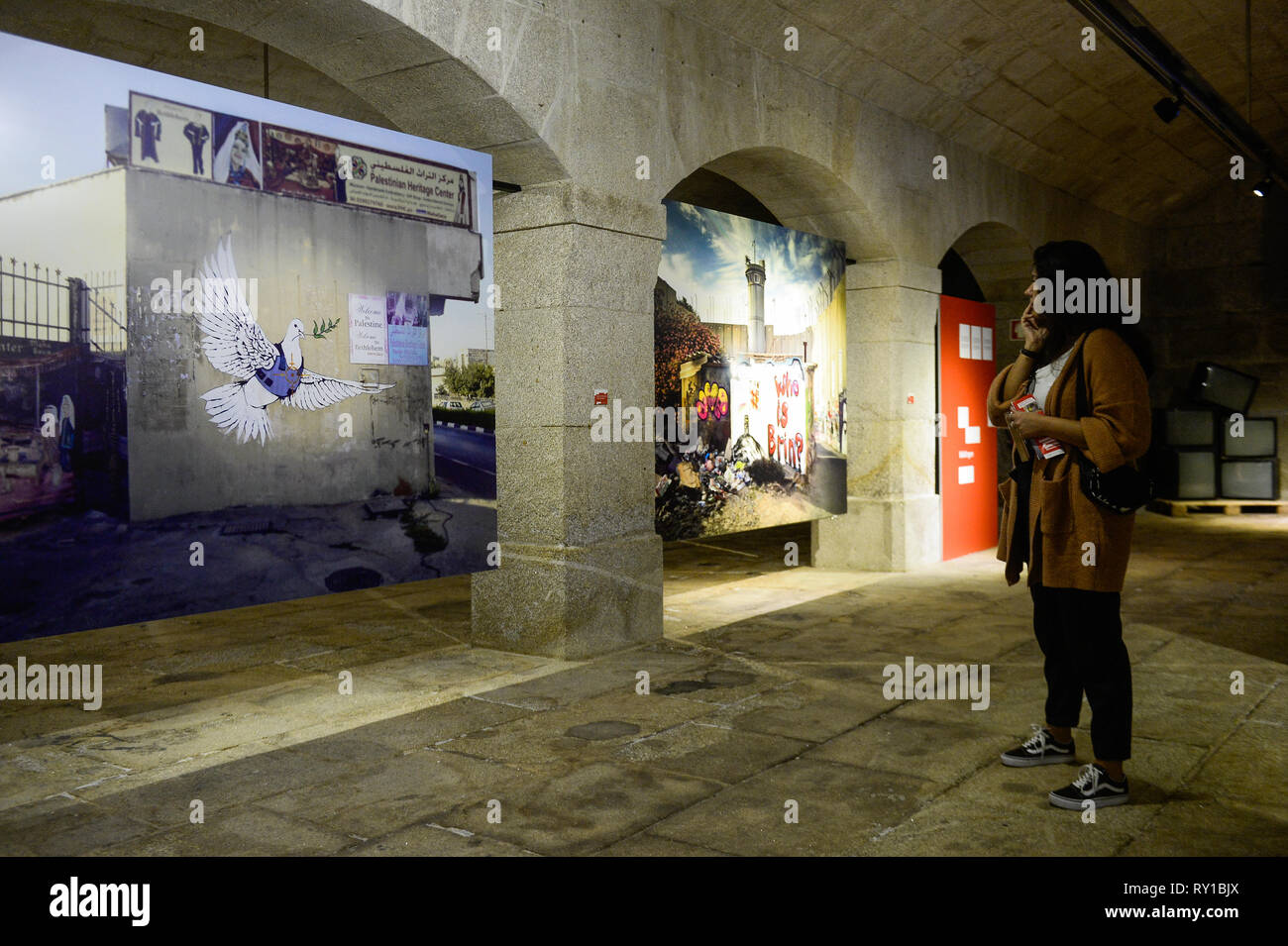 Un visitatore è vedere a piedi da "colomba e Flak Jacket' immagine durante Banksy's Dismaland e altri mostra di Alfandega centro congressi. La mostra include le immagini prese da Barry Cawston dal progetto Dismaland (2015), il ben noto parco a tema creato da Banksy, integrare altre opere che identifica l'artista come "Walled Off Hotel' (2017) o "Fiore Thrower" (2005), una delle sue opere più conosciute. Al di là di Barry immagini, la mostra si integra anche una serie di opere di giovani artisti portoghesi, servendo anche come un trampolino di lancio per nuovi nomi nell'universo urbano di arte. Foto Stock