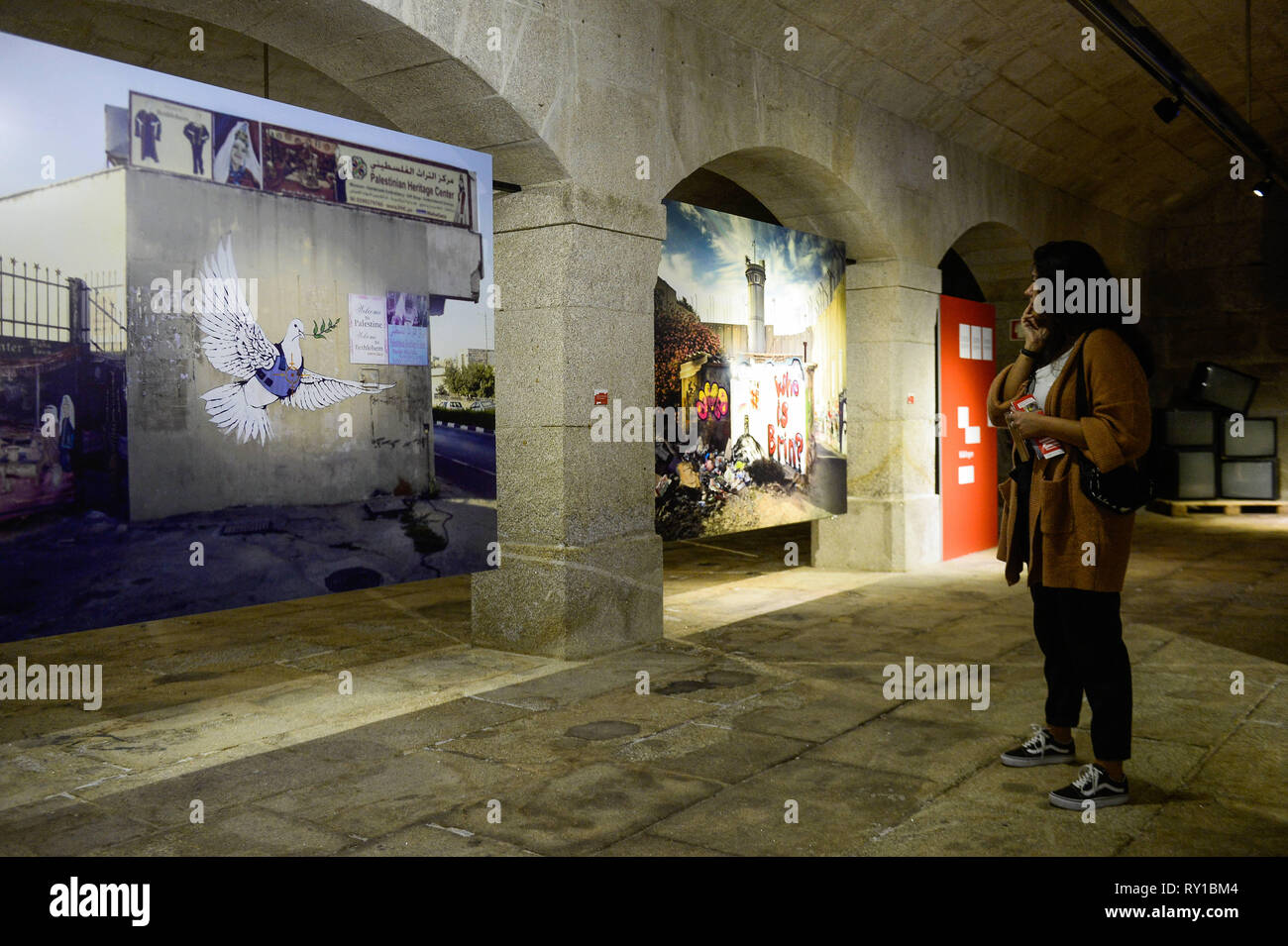 Porto, Portogallo. Decimo Mar, 2019. Un visitatore è vedere a piedi da ''disporre e Flak Jacket'' immagine durante BanksyÂ's Dismaland e altri mostra di Alfandega centro congressi. La mostra include le immagini prese da Barry Cawston dal progetto Dismaland (2015), il ben noto parco a tema creato da Banksy, integrare altre opere che identifica l'artista come ''Walled Off Hotel'' (2017) o ''Flower Thrower'' (2005), una delle sue opere più conosciute. Al di là di Barry immagini, la mostra si integra anche una serie di opere di giovani artisti portoghesi, servendo anche come un trampolino di lancio per nuovi nomi in u Foto Stock