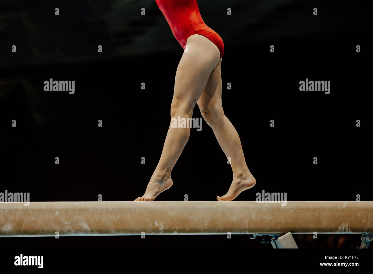 Ginnasta femmina in rosso body sul fascio di equilibrio su sfondo nero Foto Stock