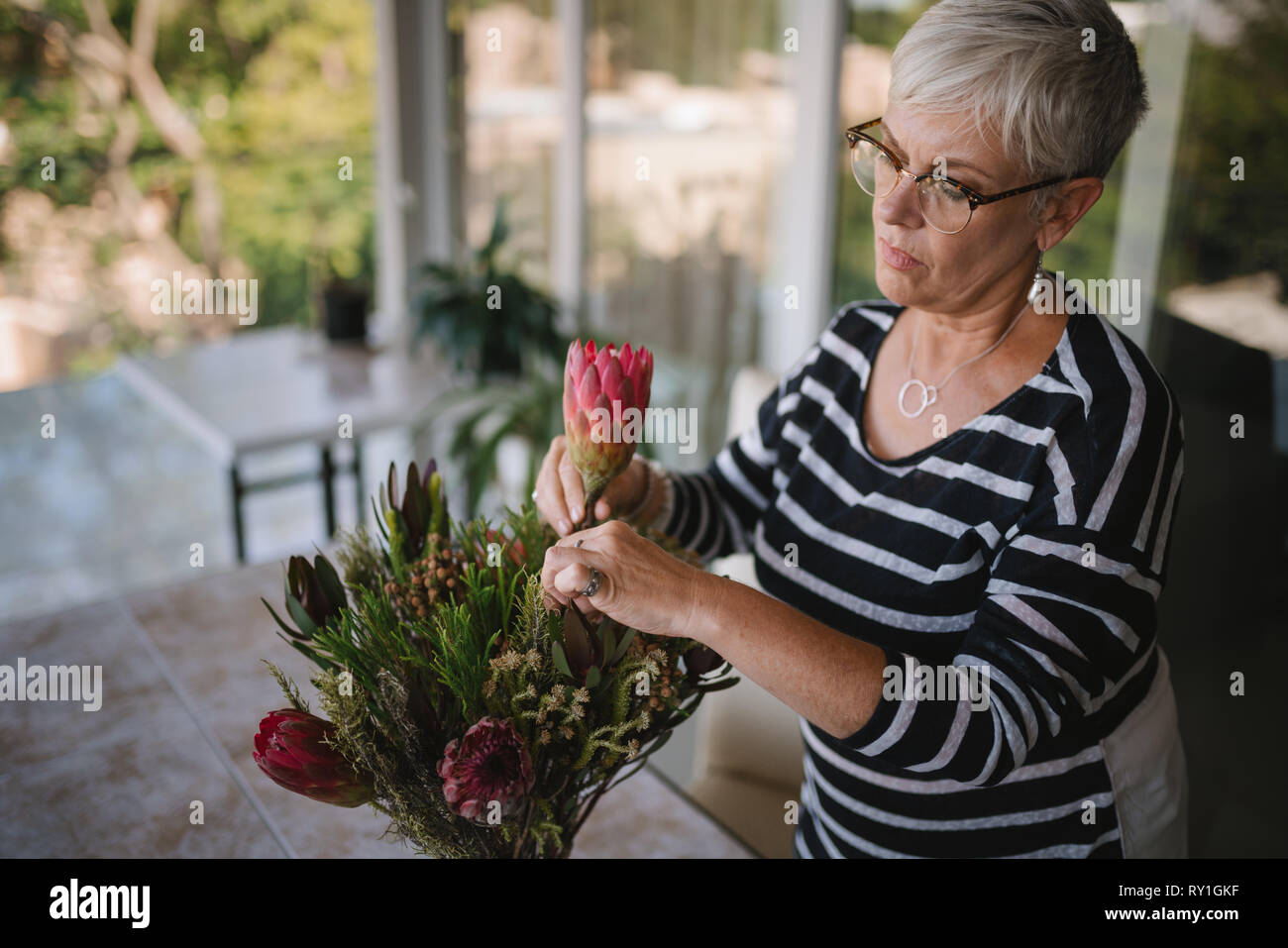 Ritratto di una donna senior aggiungendo un protea fiore per un bouquet. Donna anziana godendo disponendo dei fiori come un hobby Foto Stock
