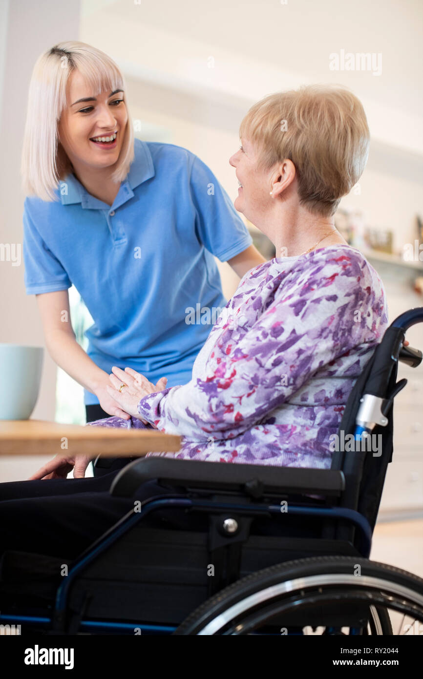 Femmina assistente di cura a parlare con il Senior donna seduta in carrozzella a casa Foto Stock