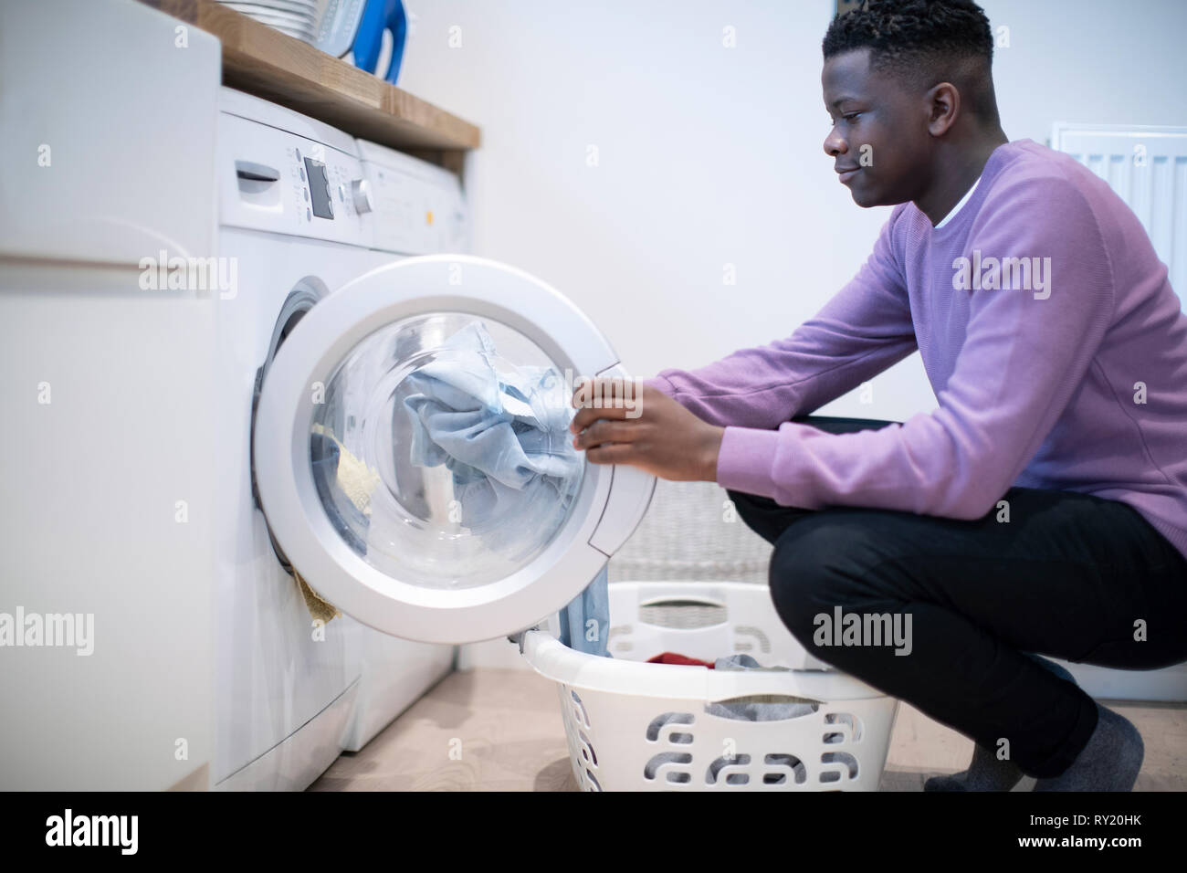 Ragazzo adolescente aiutando con lavori domestici a casa lo svuotamento della macchina di lavaggio Foto Stock