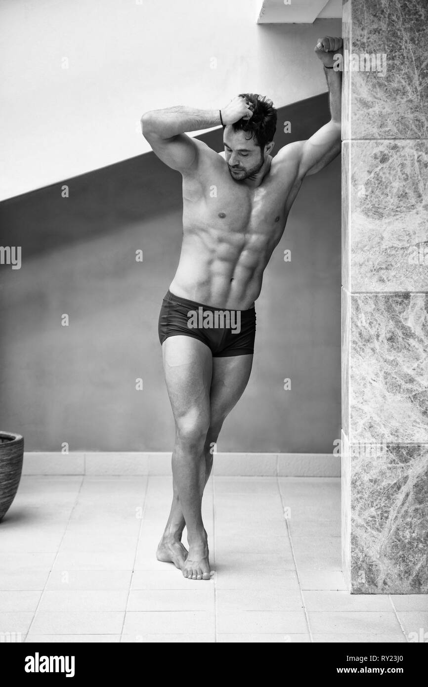 Ritratto di un giovane fisicamente l uomo che mostra il suo ben addestrato corpo mentre indossa pantaloncini Sport - Atletico muscolare Bodybuilder Modello di Fitness in posa Foto Stock