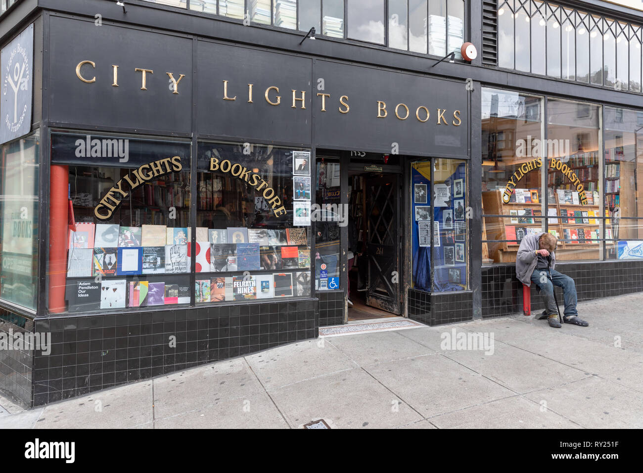 Luci della città libri, negozio di fronte; senzatetto uomo appoggiato dall ingresso; San Francisco, California, Stati Uniti d'America Foto Stock