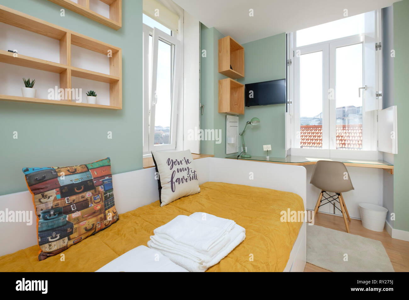Decorato in maniera colorata piccolo appartamento camera da letto con letto singolo, grandi finestre e una scrivania con sedia Foto Stock