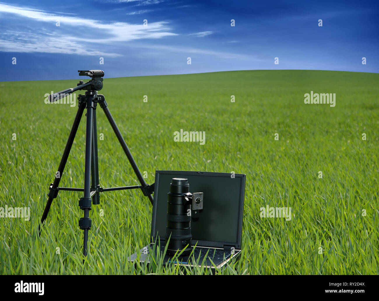 Apparecchiature fotografiche e portatile su un campo verde, cielo blu e nuvole bianche in background Foto Stock