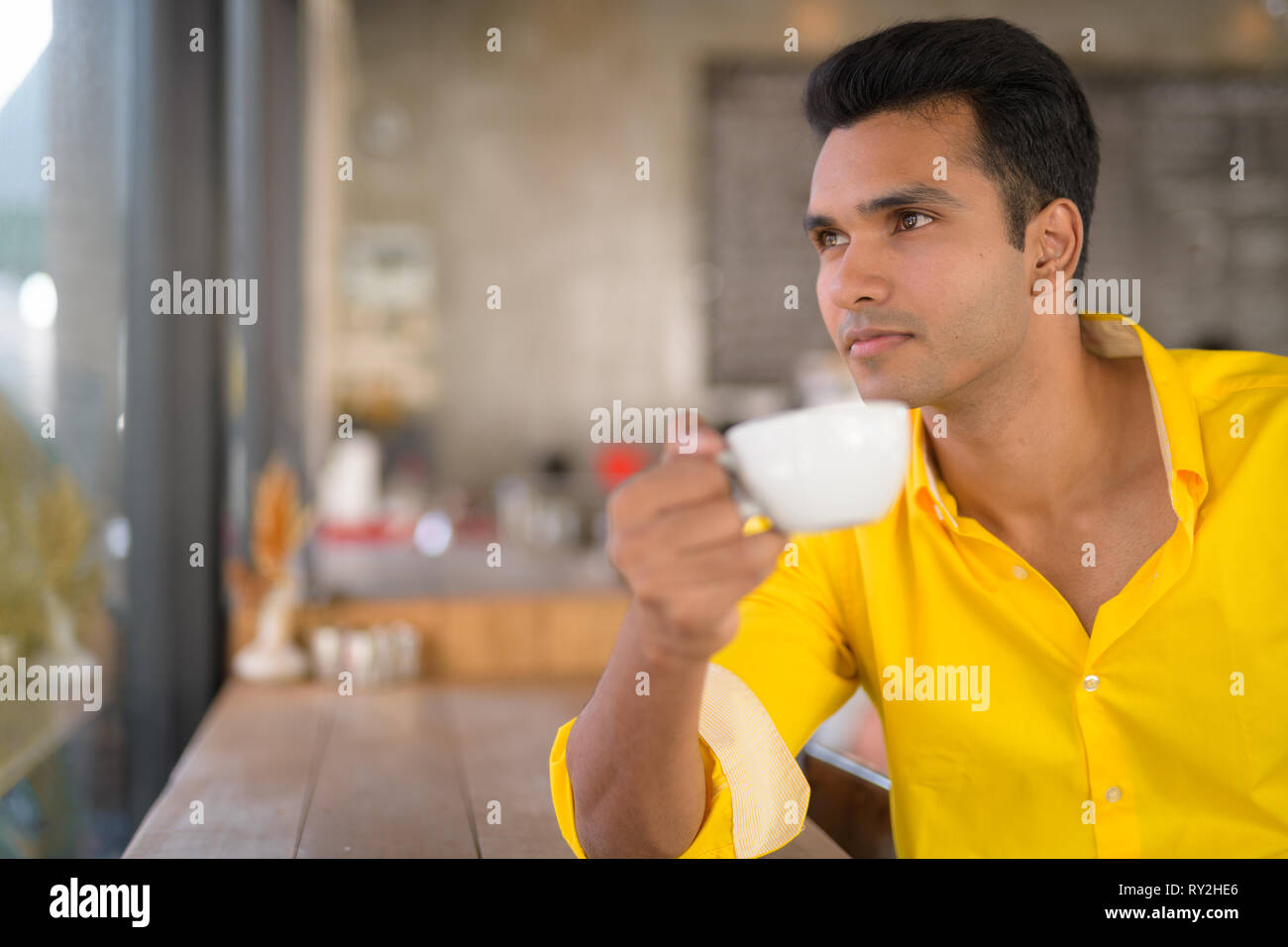 Bel giovane uomo indiano di bere il caffè guardando fuori attraverso la finestra al cafe Foto Stock
