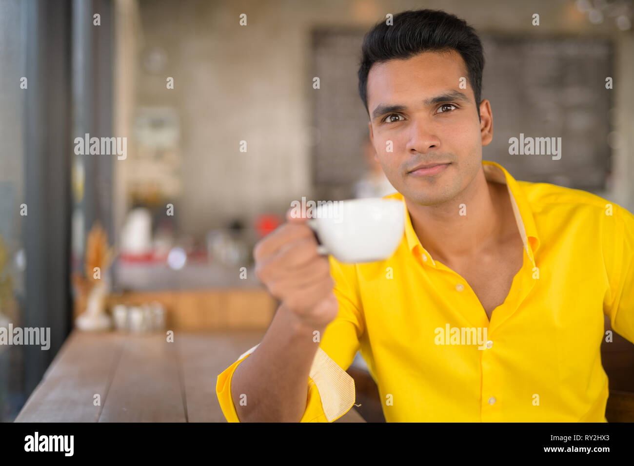 Bel giovane uomo indiano di bere il caffè dalla finestra al coffee shop Foto Stock