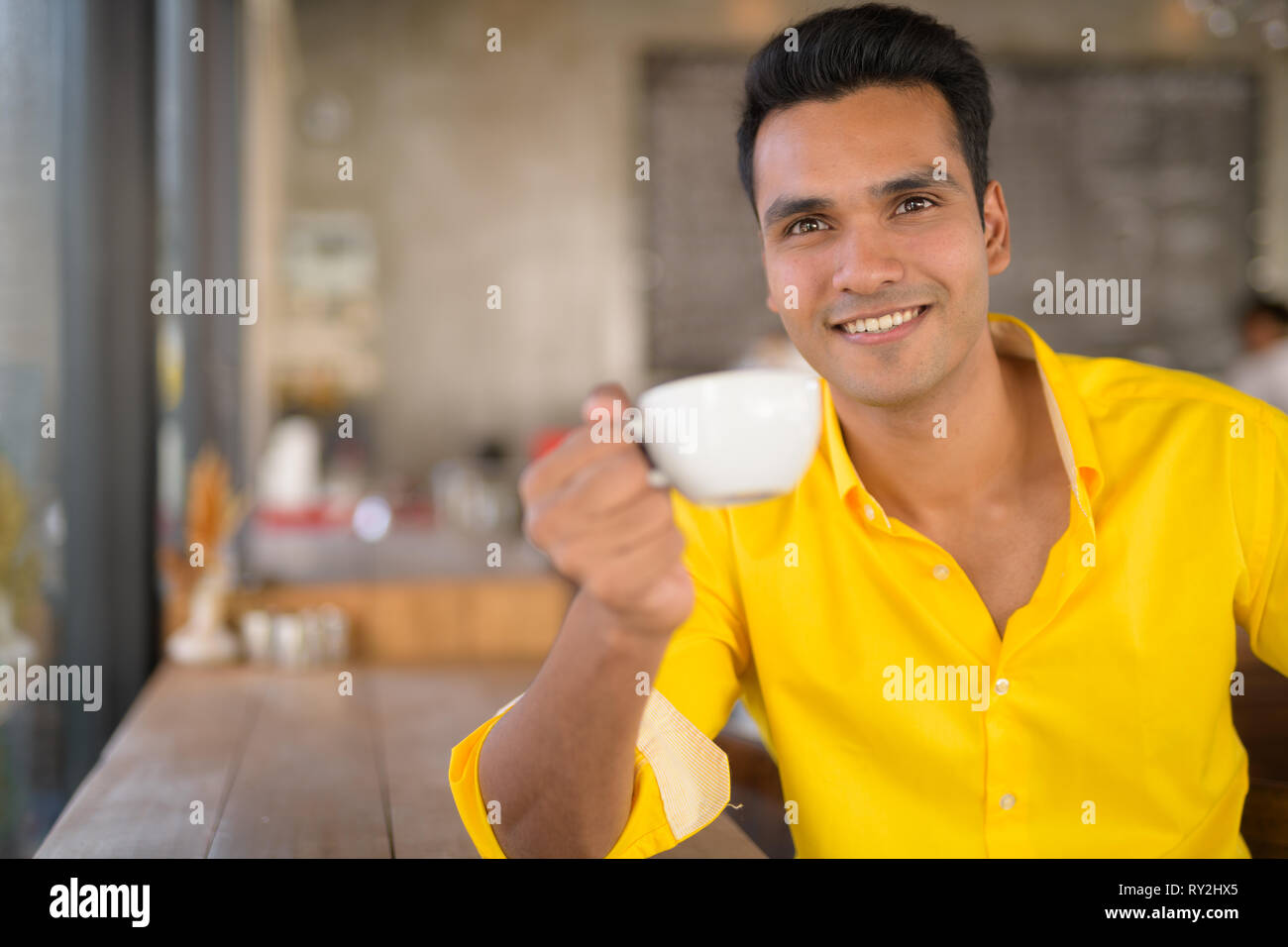 Giovani felici uomo indiano di bere il caffè dalla finestra al coffee shop Foto Stock