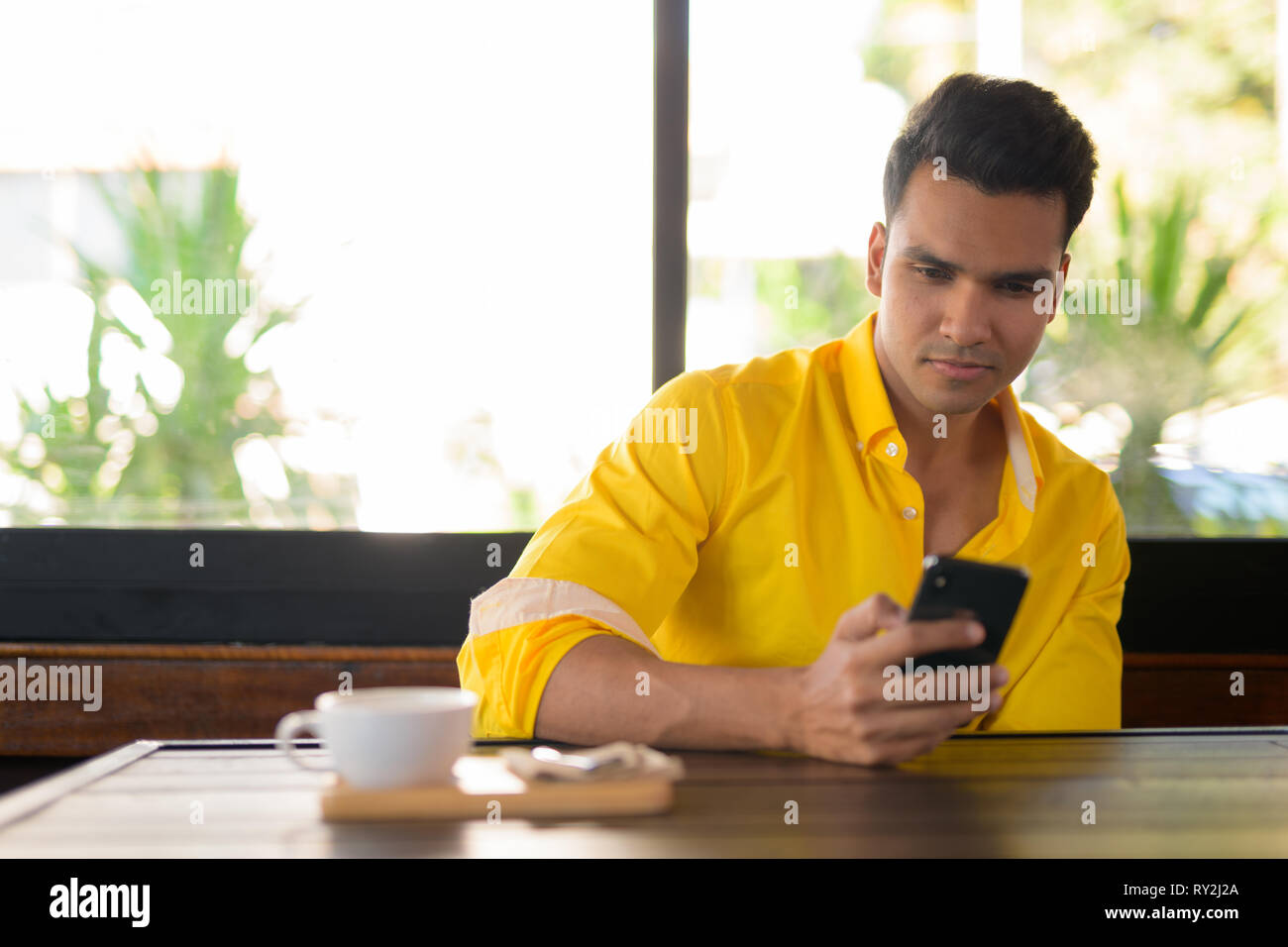 Bel giovane uomo indiano usando il telefono presso la caffetteria Foto Stock