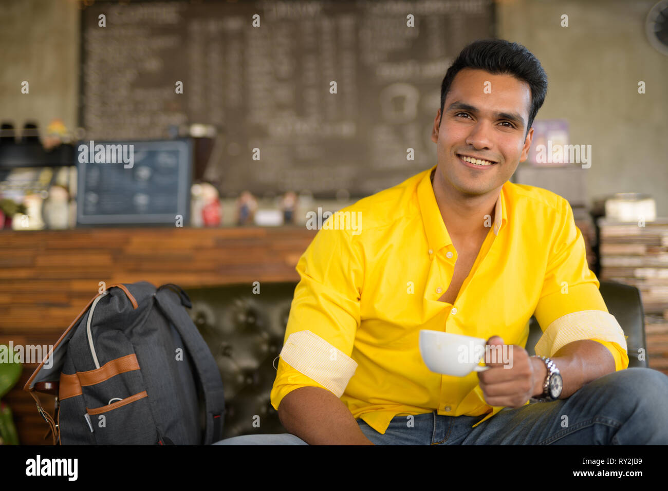 Giovani indiani felici uomo seduto e di bere il caffè presso la caffetteria Foto Stock