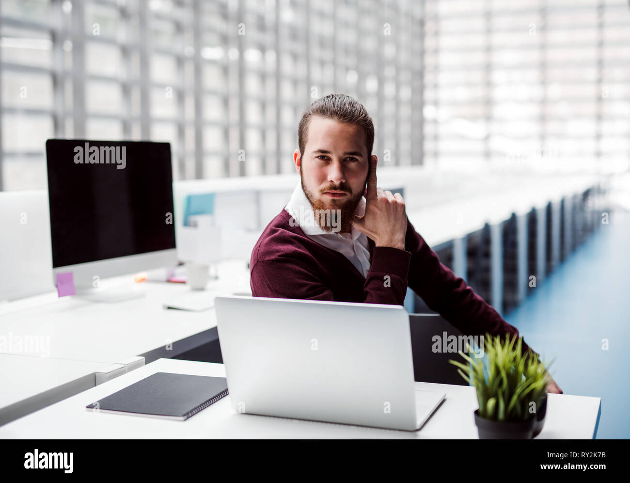Un giovane imprenditore serio con il computer portatile in ufficio, guardando la fotocamera. Foto Stock