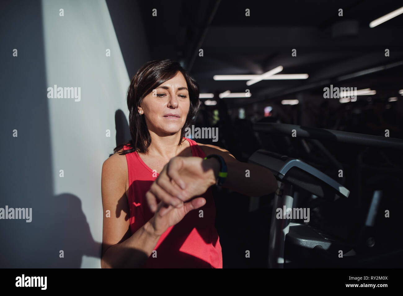 Un senior donna in palestra riposo dopo fare esercizio, controllo del tempo. Foto Stock