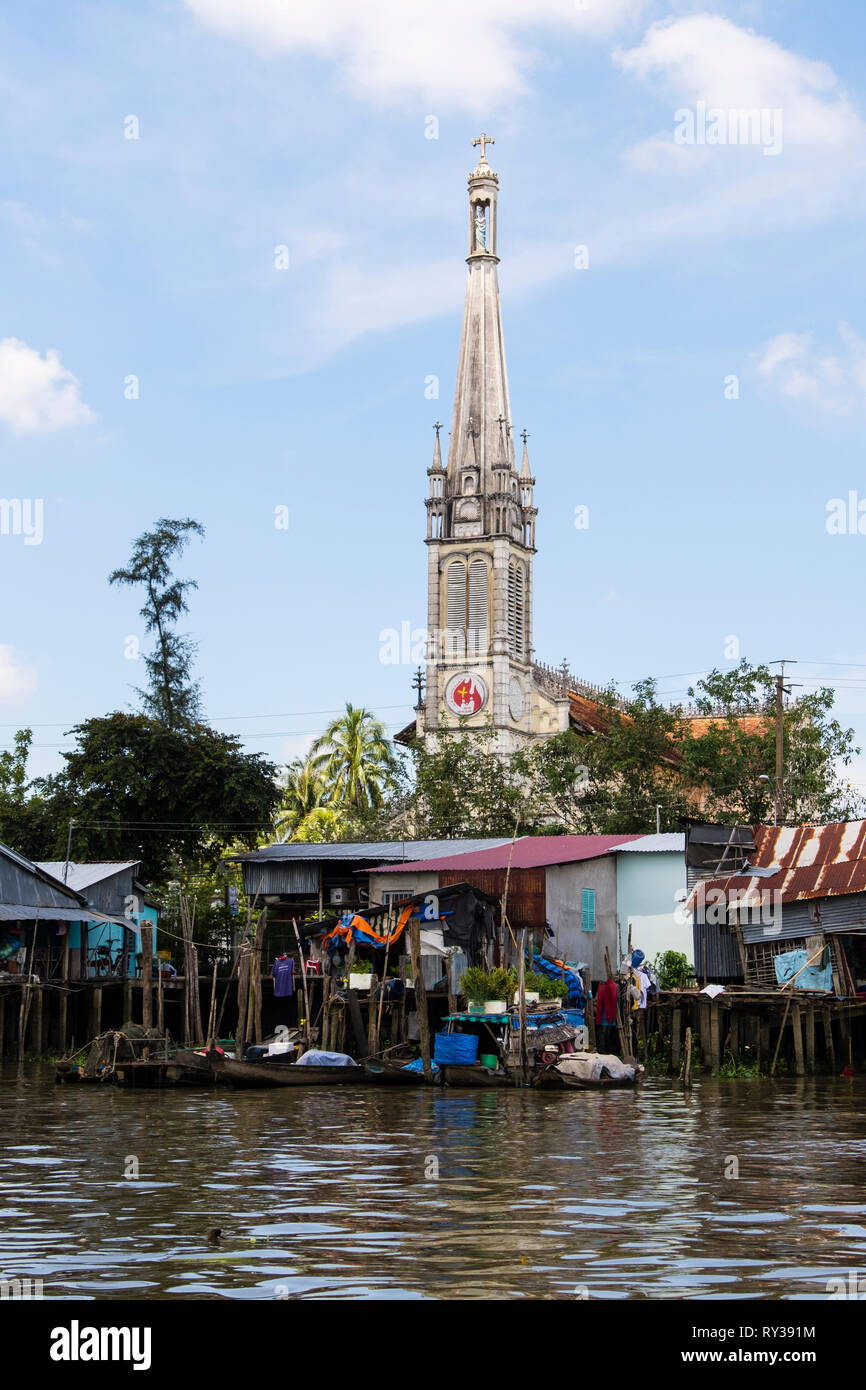 Xx secolo cattedrale cattolica Chiesa dietro tipico stagno vietnamita shack palafitte sul lungofiume del Co Chien fiume nel Delta del Mekong. In Cai Be Vietnam Foto Stock