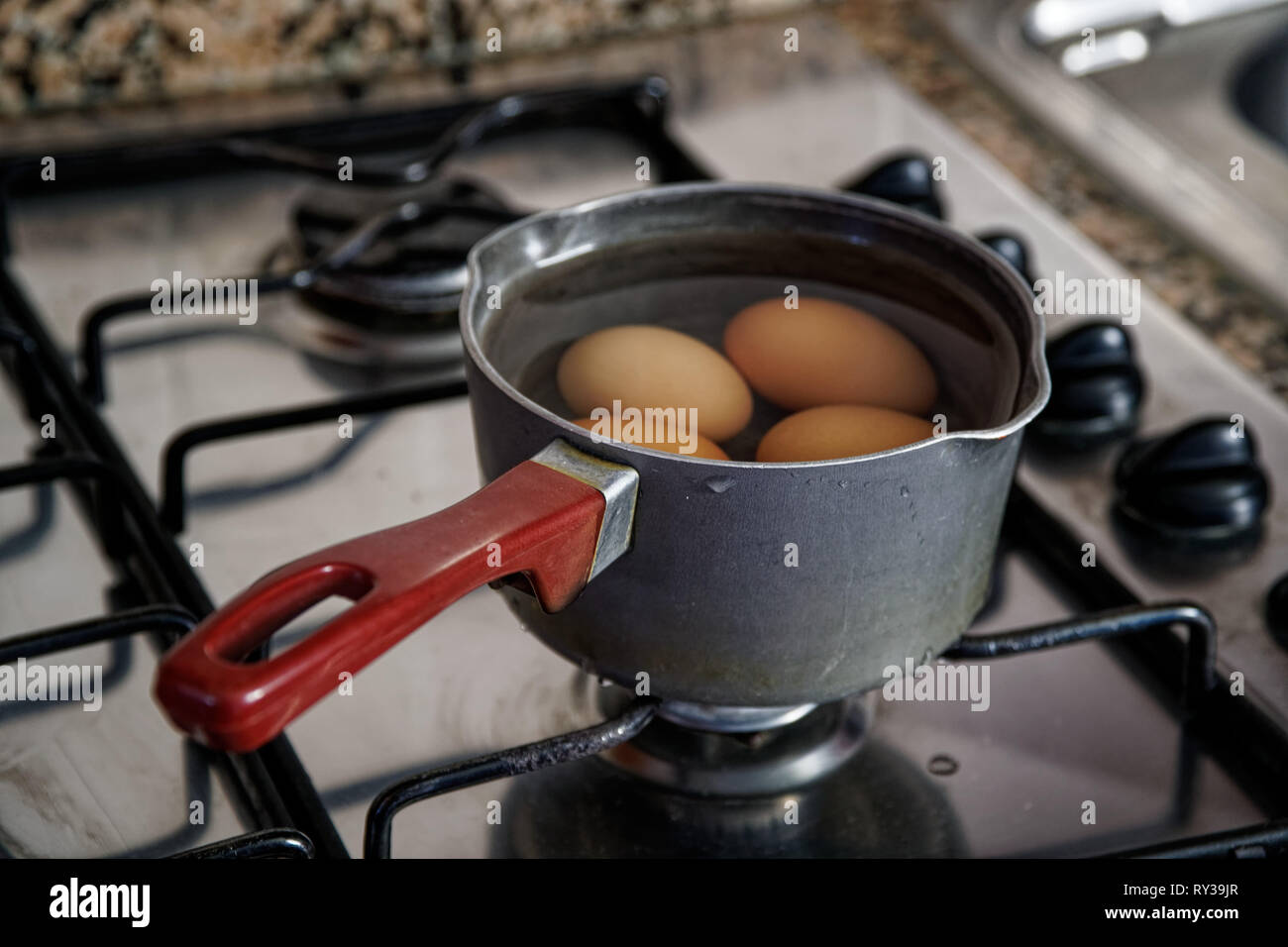 Uova sode nel mestolo di acqua sul fornello da cucina Foto stock - Alamy