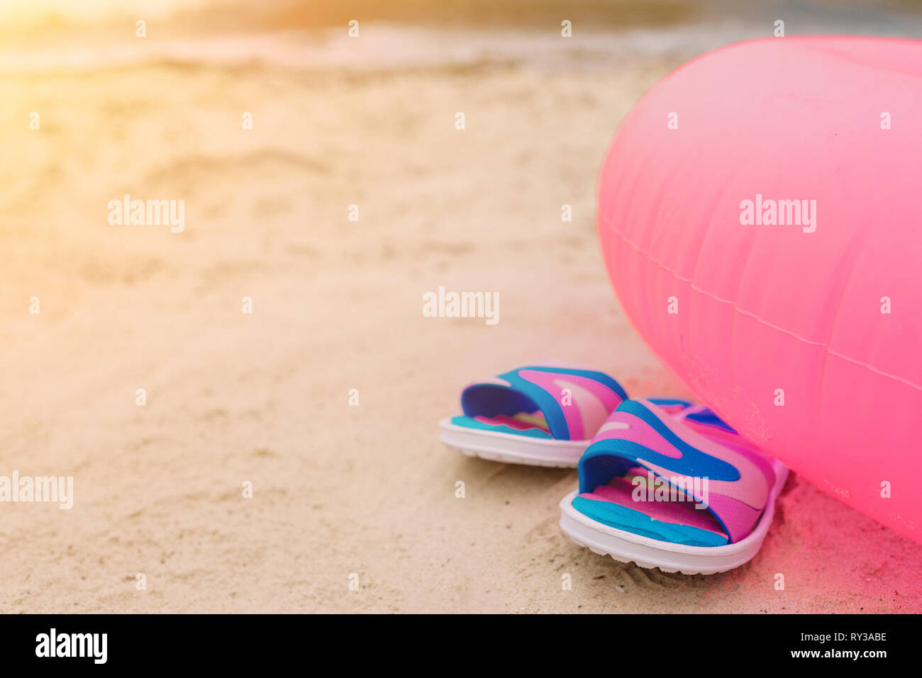 Flip-flop giacente sulla spiaggia sotto il nuoto rosa cerchio. La vacanza estiva concetto. Sole risplende luminosa. Vista di taglio. Foto Stock