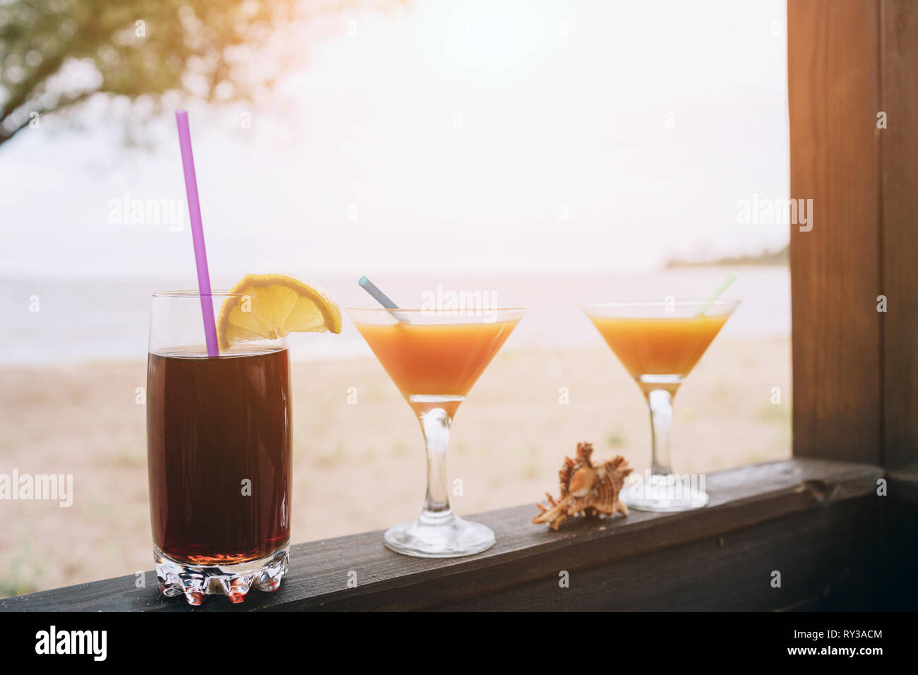 Concetto di estate: fresco cocktail esotici sul bordo di legno. Guscio compreso tra bicchieri. Cola con paglia e limone. La vita sull'isola. Il paradiso. Foto Stock