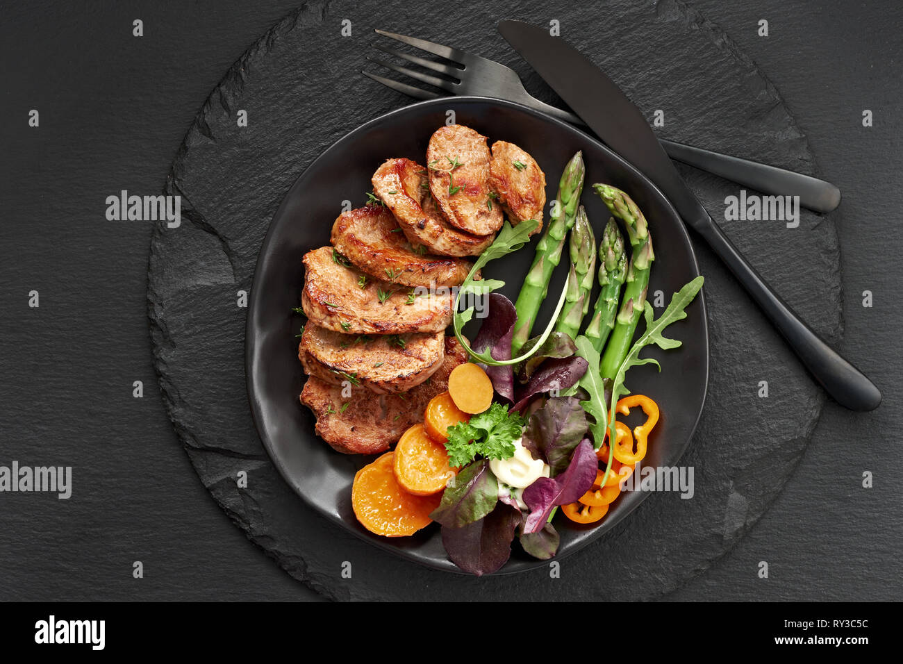 Frittura di fette di carne di manzo, patate dolci, asparagi e insalata mista sulla piastra nera impostata per il pasto di ardesia scura scheda di pietra Foto Stock