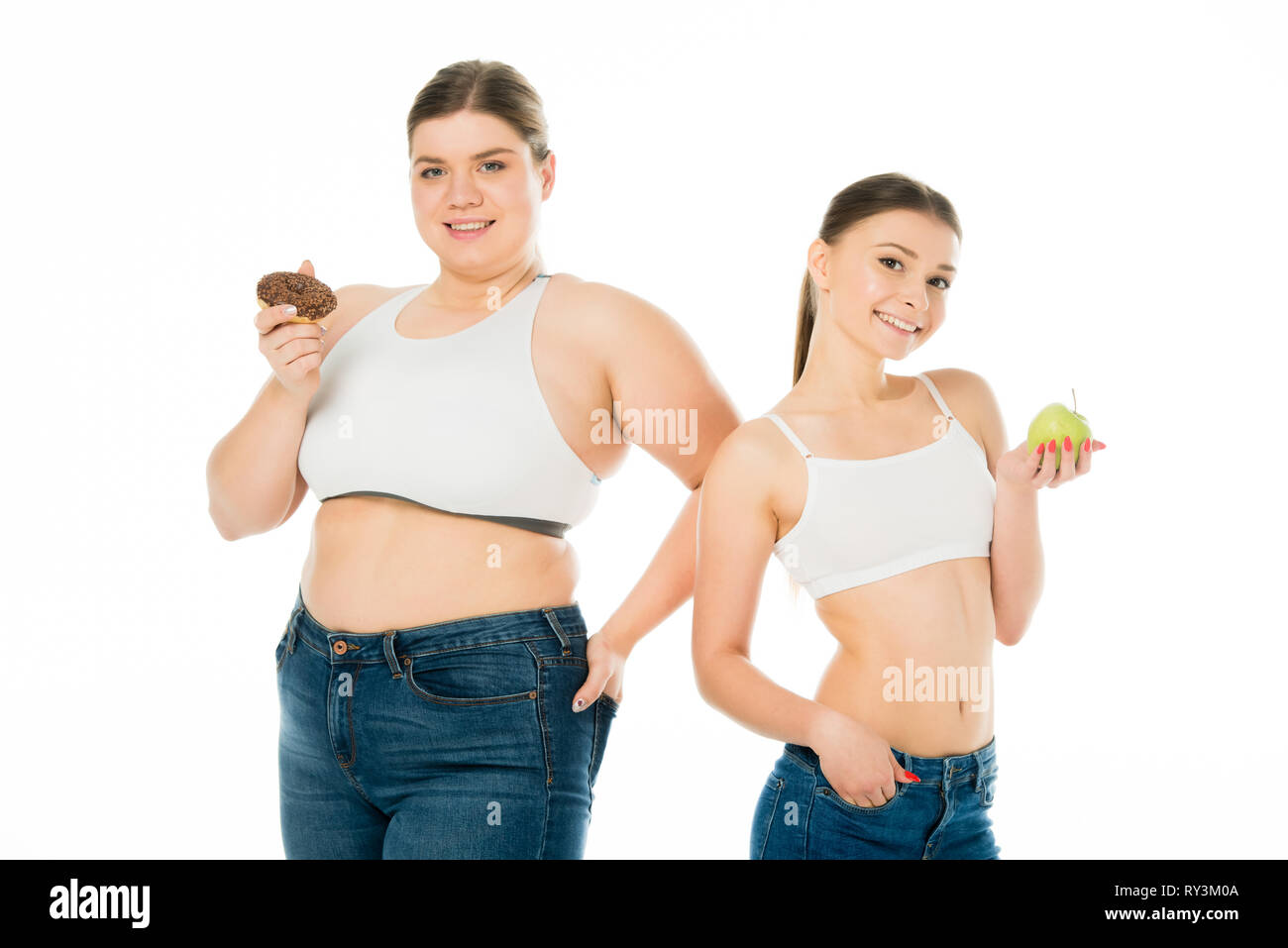 Felice sottile e sovrappeso ragazze in posa insieme a ciambella e mela verde isolato su bianco Foto Stock