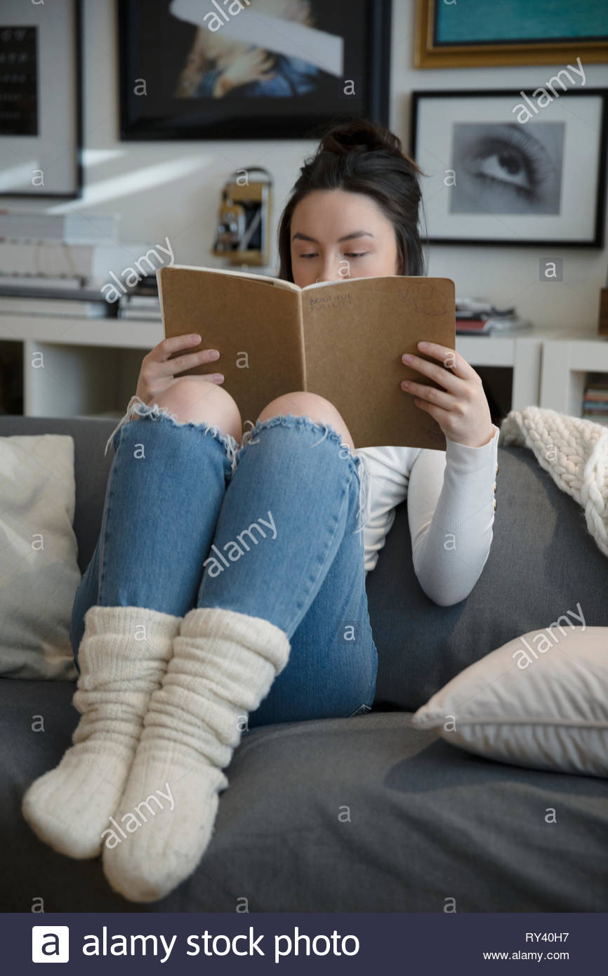 Accogliente giovane donna lettura sul divano Foto Stock