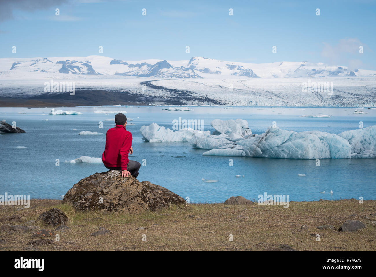 L'uomo traveler in giacca rossa si trova sulle sponde di un lago. Paesaggio estivo con laguna glaciale, di ghiacciai, iceberg nel sud-est dell' Islanda, Europa Foto Stock