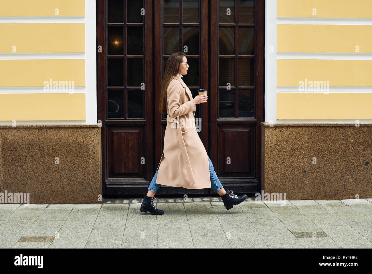 Giovane donna a piedi la strada con un caffè per andare e un telefono cellulare. Foto Stock