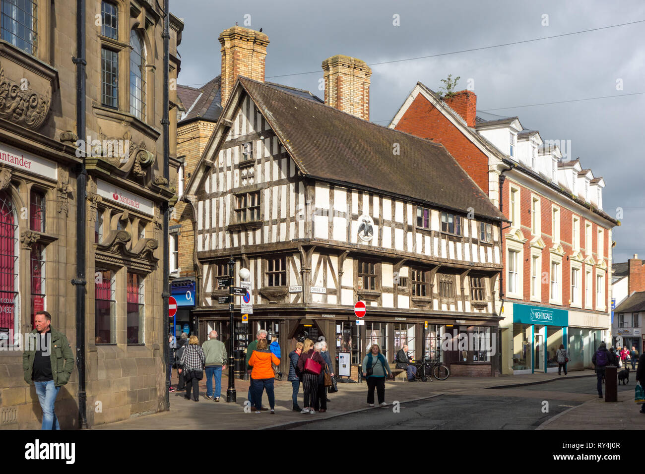 La gente fa shopping sulla High Street nella città di mercato di Shropshire di Oswestry con una vista della metà bianca e nera del palazzo di Llwyd. Foto Stock