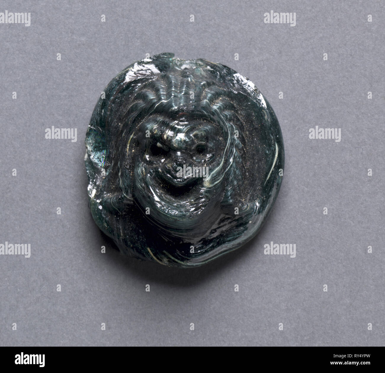 Maschera di fumetti, c. I secolo d.c. La Grecia, periodo greco-romano, fine dinastia tolemaica all Impero Romano. In vetro verde scuro; diametro: 3,6 cm (1 7/16 in.), in totale: 1,7 cm (11/16 in Foto Stock