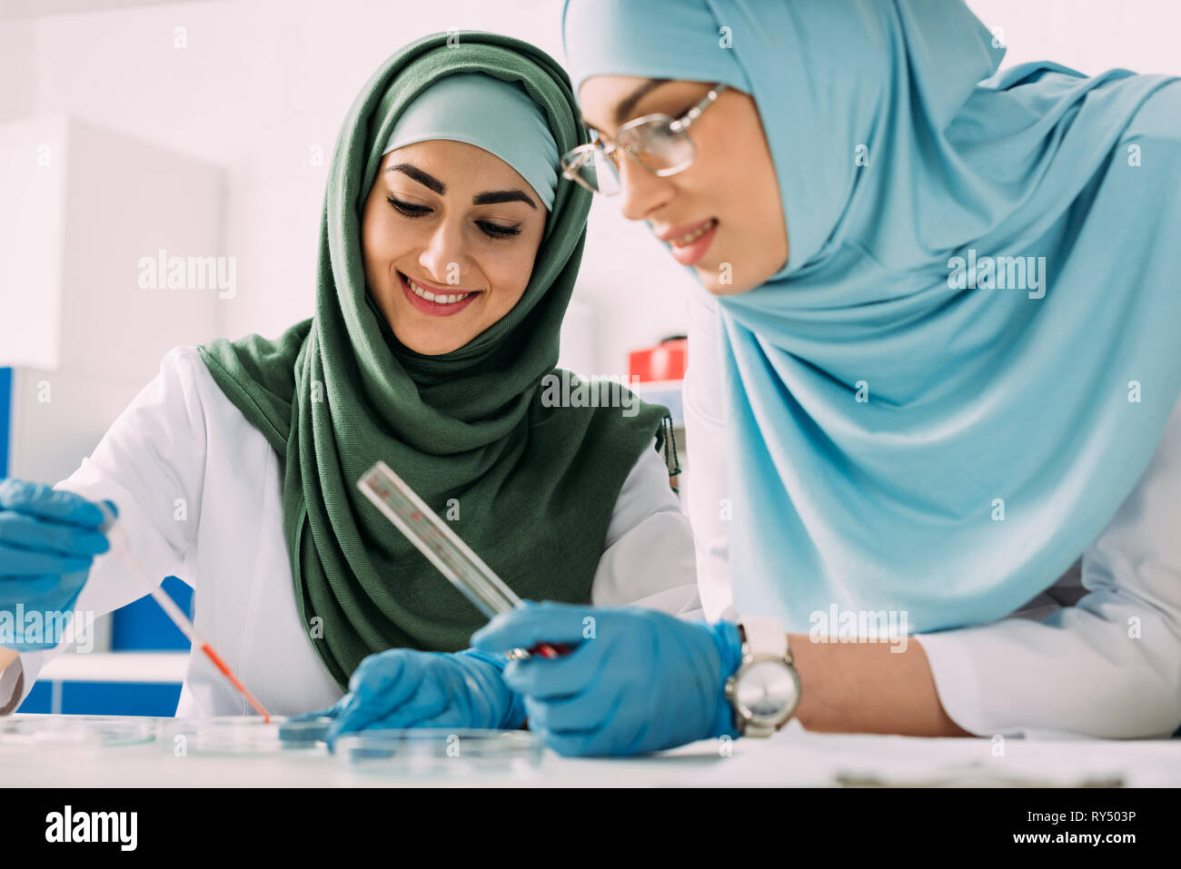 Donna sorridente scienziati musulmani tenendo la pipetta e la provetta di vetro durante la sperimentazione in laboratorio chimico Foto Stock