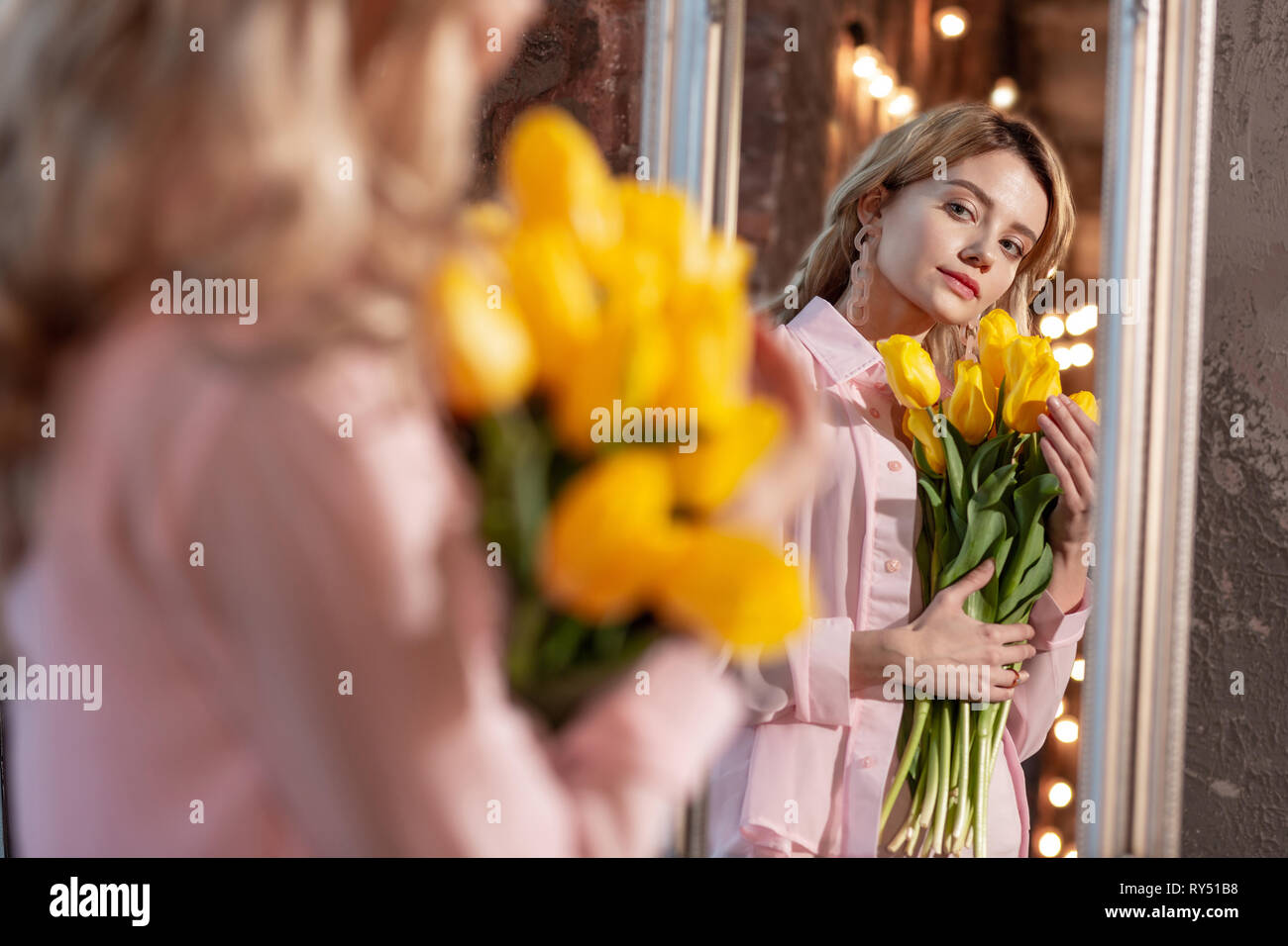 Attraente donna che indossa camicetta rosa azienda fiori gialli Foto Stock