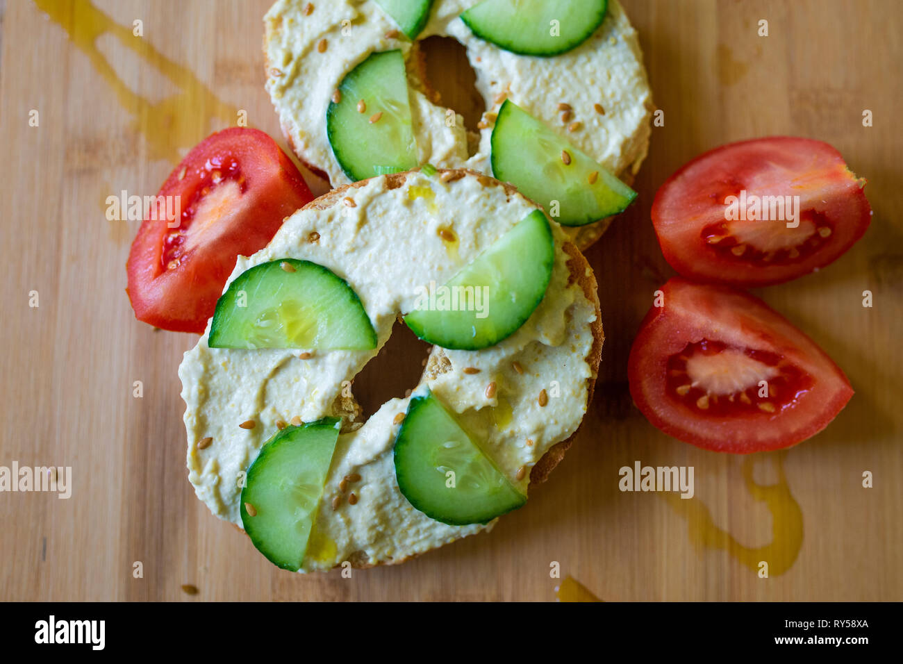 Cibo vegan. Un bagel con hummus, humous, hommous e cetriolo, vegano vegetariano, cibo sano la colazione o il pranzo su una tavola di legno Foto Stock