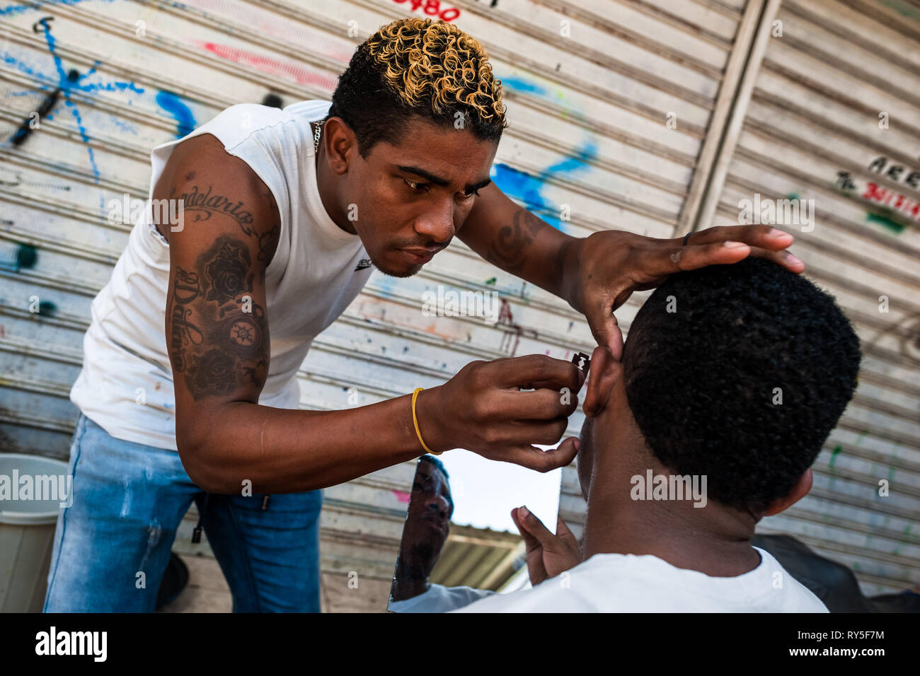 Un giovane uomo colombiano rade un amico con la barba con la lama di un rasoio nel mercato di Bazurto, Cartgena, Colombia. Foto Stock