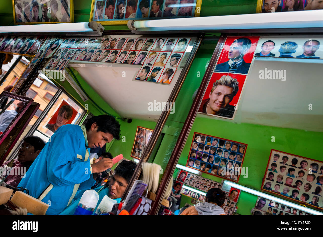 Un giovane boliviano parrucchiere taglia di un cliente in capelli in un negozio di barbiere di El Alto, la Bolivia, il 11 febbraio 2014. Foto Stock