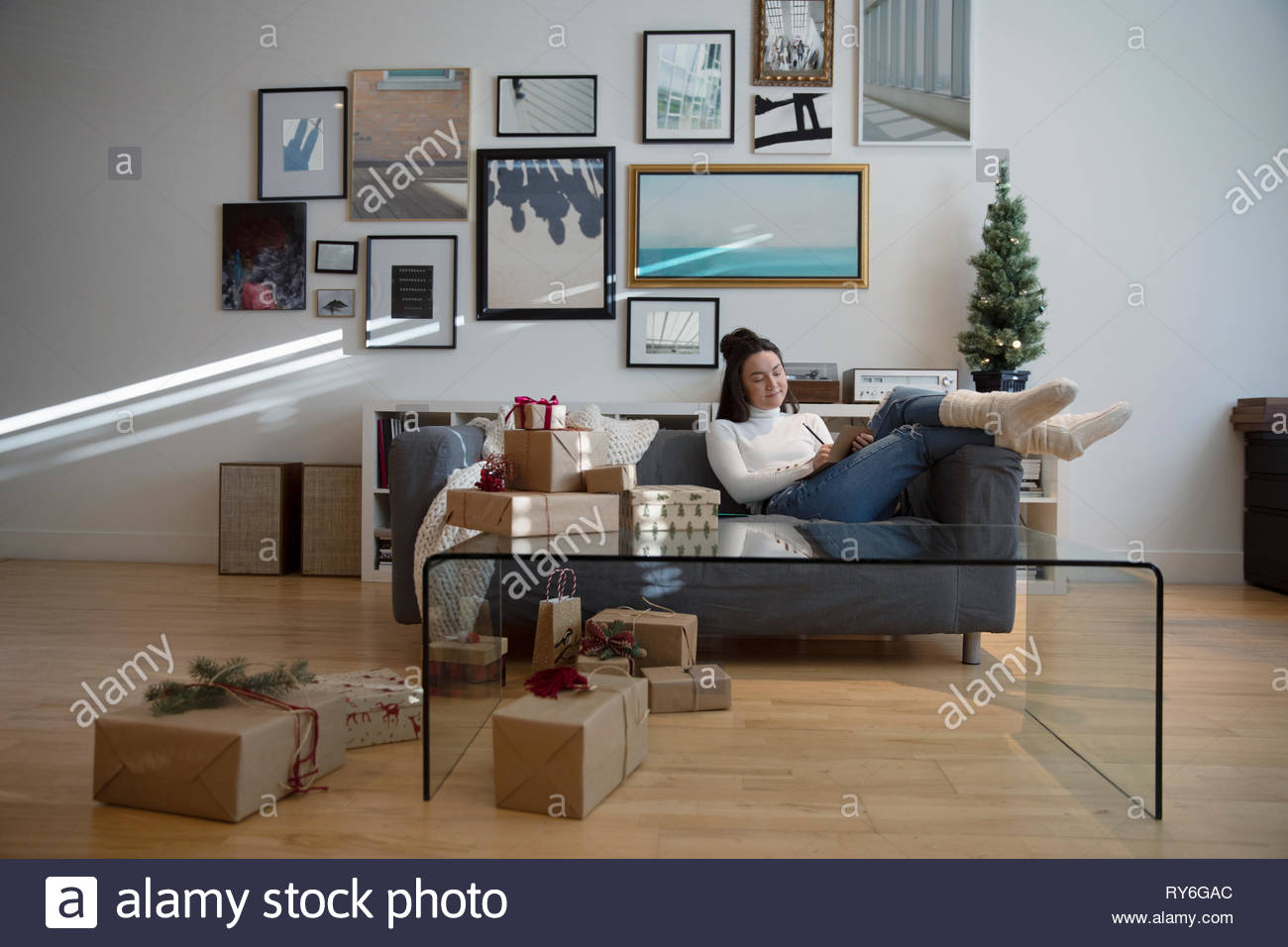 Accogliente giovane donna incarto di regali di Natale in salotto Foto Stock