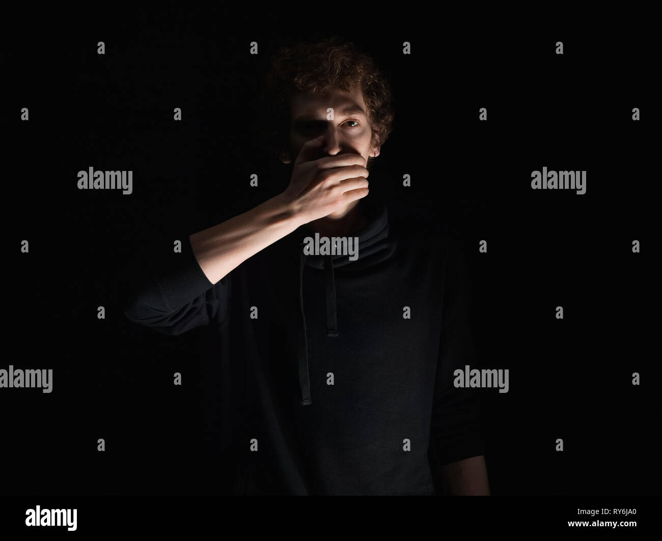 Ritratto di uomo con la mano che copre la bocca in piedi su sfondo nero Foto Stock