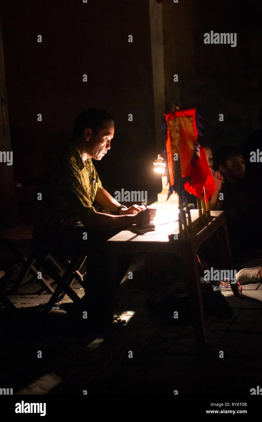 Uomo asiatico la scrittura a mano a lume di candela sulla tavola di piccole dimensioni - Hoi An, Vietnam Foto Stock