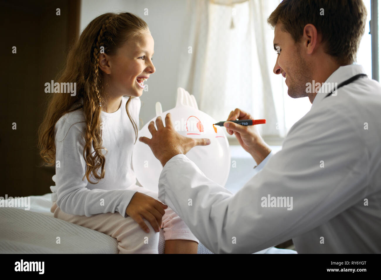 Giovane medico il disegno di una faccia su un palloncino per un paziente giovane. Foto Stock