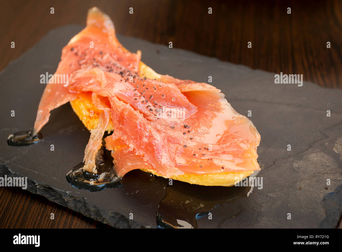 Primo piano di un pezzo di deliziosi salmone guarnito con olio e spezie serviti a bordo Foto Stock